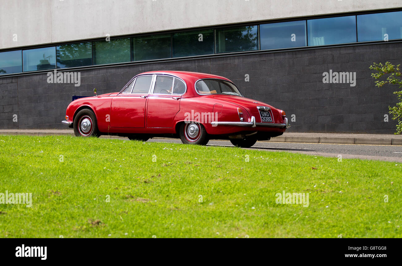 A red vintage 1960`s Jaguar 420 saloon car traveling past the Abertay University building in Dundee, UK Stock Photo